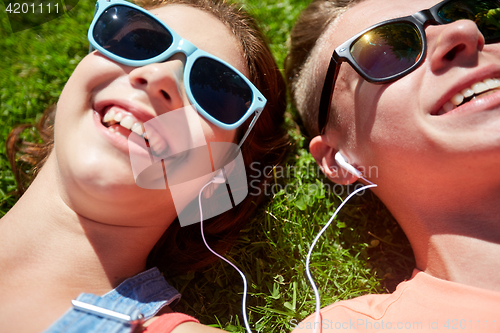 Image of happy teenage couple with earphones lying on grass