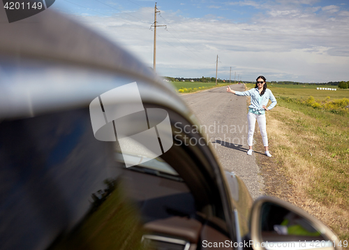 Image of woman hitchhiking and stopping car with thumbs up