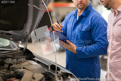 Image of auto mechanic with clipboard and man at car shop