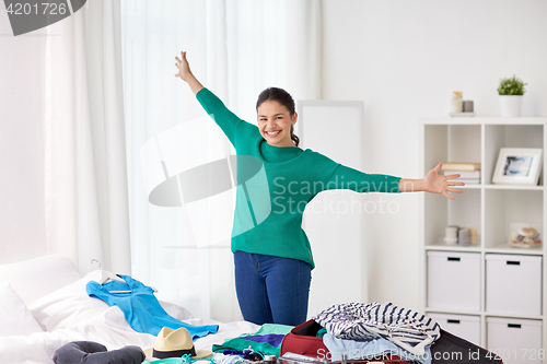 Image of happy woman packing travel bag at home
