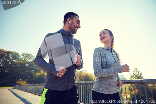 Image of happy couple with earphones running outdoors