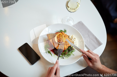 Image of woman with smartphone eating salad at restaurant