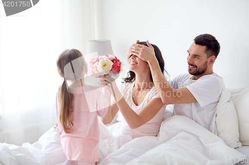 Image of happy girl giving flowers to mother in bed at home