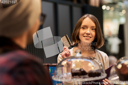 Image of happy woman with credit card buying cakes at cafe