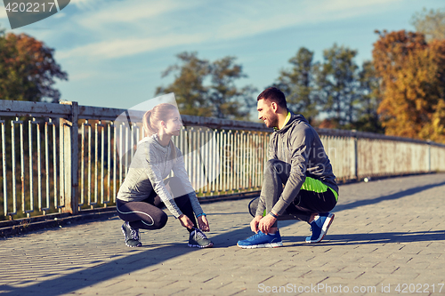 Image of smiling couple tying shoelaces outdoors