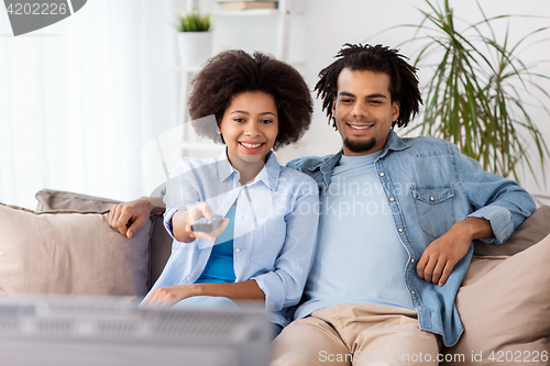 Image of smiling couple with remote watching tv at home