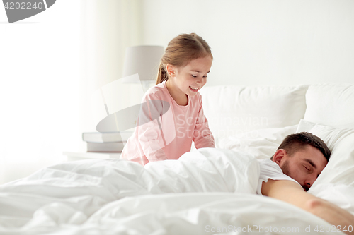 Image of little girl waking her sleeping father up in bed