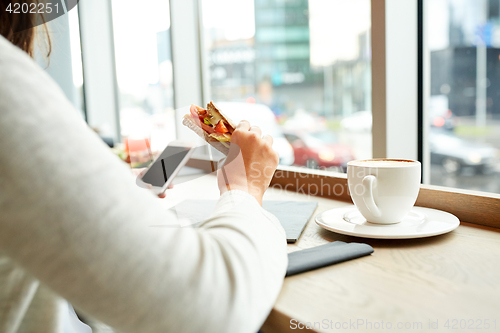 Image of woman with smartphone and sandwich at restaurant