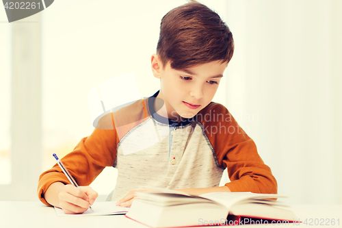 Image of student boy with book writing to notebook at home