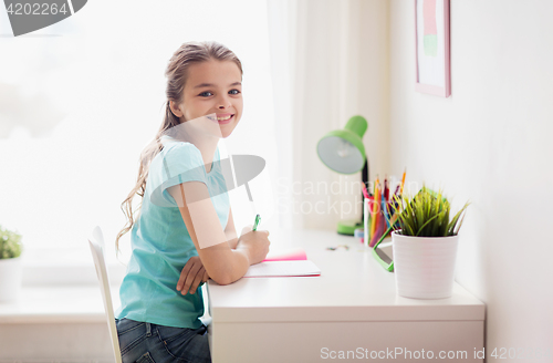 Image of happy girl with book writing to notebook at home