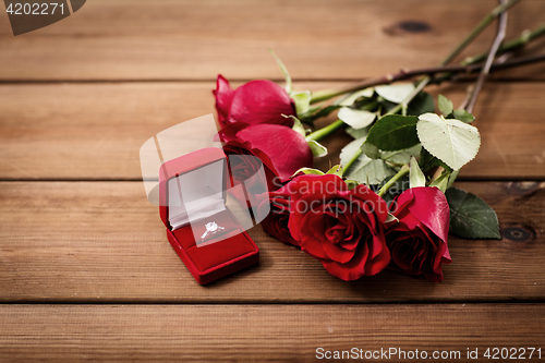 Image of close up of diamond engagement ring and red roses