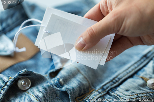 Image of close up of hand holding price tag of denim jacket