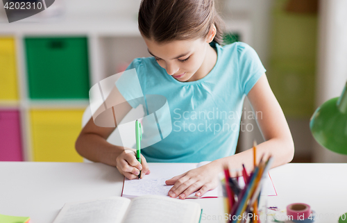 Image of happy girl with book writing to notebook at home