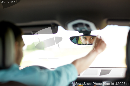 Image of man driving car adjusting rearview mirror