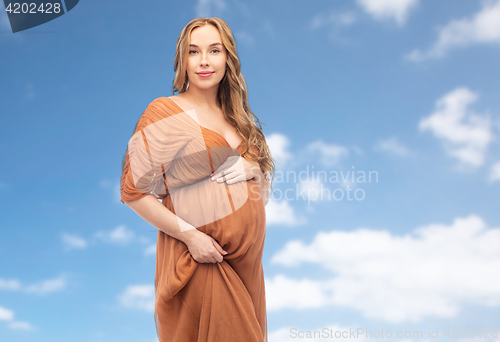 Image of happy pregnant woman touching her belly over sky