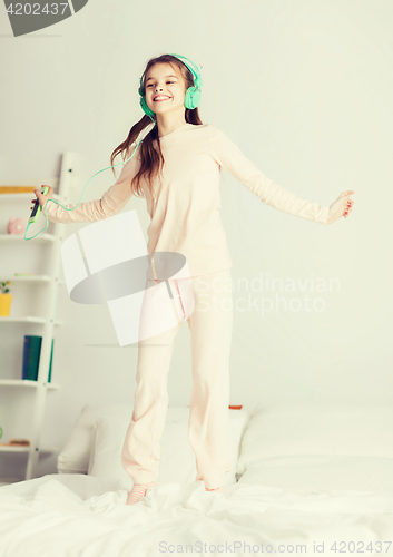 Image of girl jumping on bed with smartphone and headphones