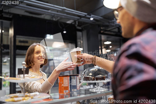 Image of seller giving coffee cup to woman customer at cafe