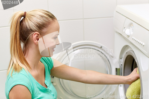 Image of happy woman putting laundry into washer at home