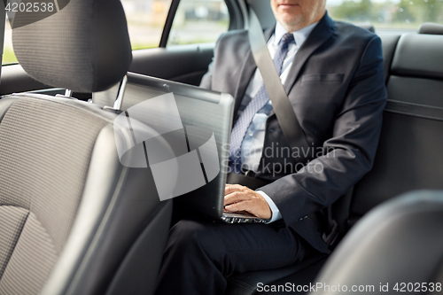 Image of senior businessman with laptop driving in car