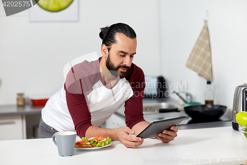 Image of man with tablet pc eating at home kitchen