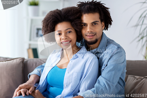Image of happy couple sitting on sofa and hugging at home