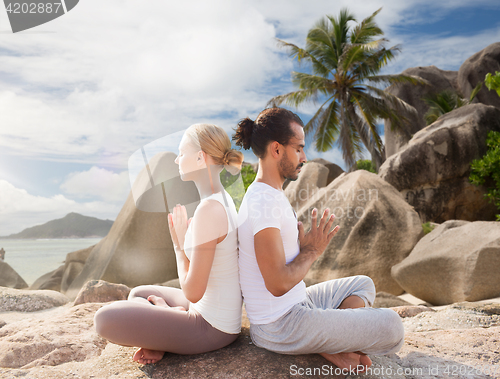 Image of smiling couple making yoga exercises on beach