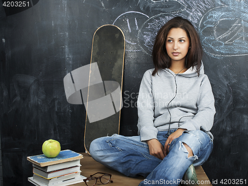 Image of young cute teenage girl in classroom at blackboard seating on table smiling, modern hipster concept