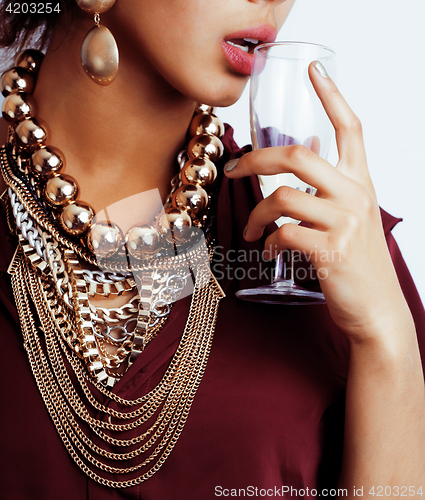 Image of young african-american woman drinking champagne, holding glass, wearing lot of golden jewelry 