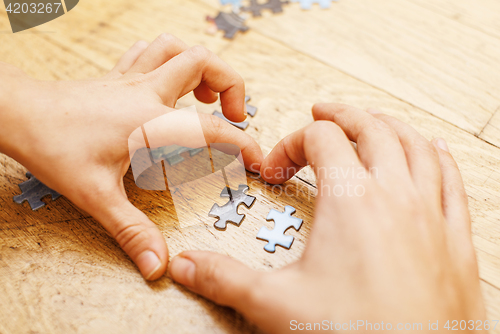 Image of little kid playing with puzzles on wooden floor together with parent, lifestyle people concept, loving hands to each other, warm wooden interior