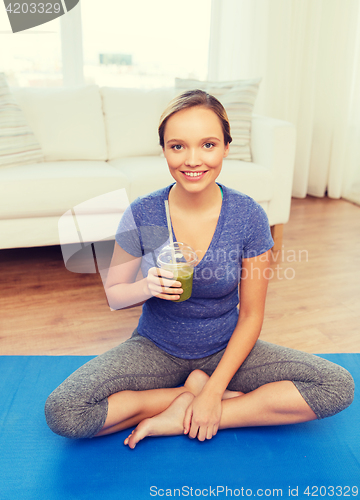 Image of happy woman with smoothie sitting on mat at home