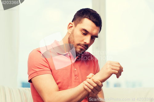 Image of unhappy man suffering from pain in hand at home