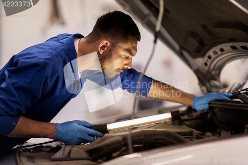 Image of mechanic man with lamp repairing car at workshop