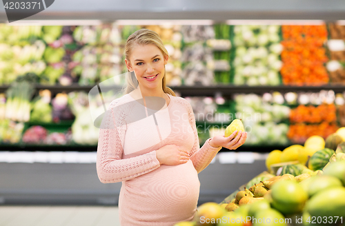 Image of happy pregnant woman with pear at grocery store