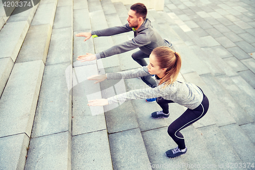 Image of couple doing squats on city street stairs