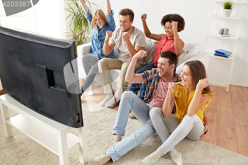 Image of happy friends with remote watching tv at home