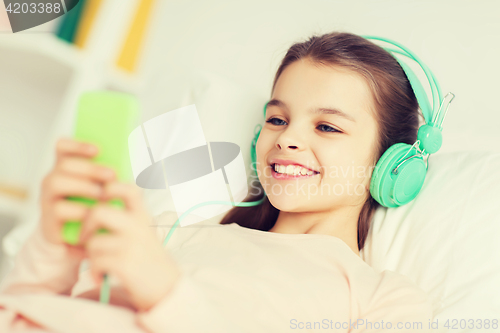 Image of happy girl lying in bed with smartphone at home