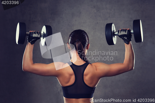 Image of young woman flexing muscles with dumbbells in gym