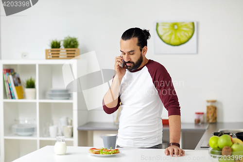 Image of man calling on smartphone and eating at home