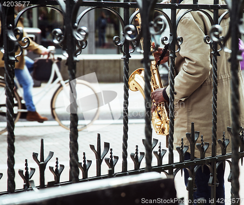 Image of african street musician playing jazz on saxophone throw lattice 
