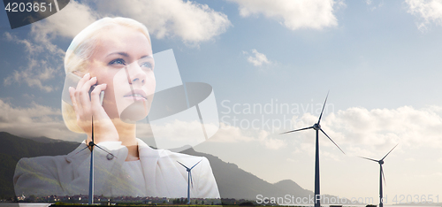 Image of businesswoman with smartphone over wind turbines