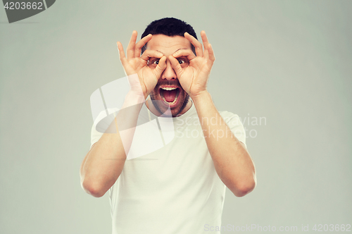 Image of man making finger glasses over gray background