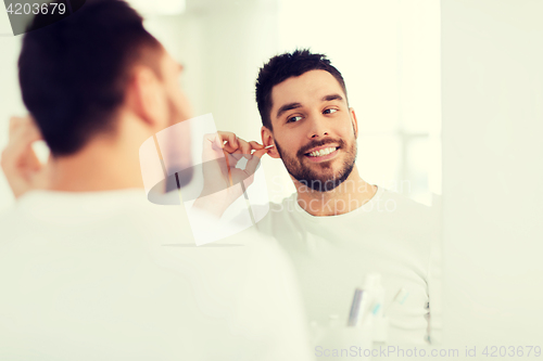 Image of man cleaning ear with cotton swab at bathroom