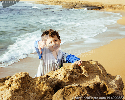 Image of little cute boy on sea coast thumbs up playing with rocks