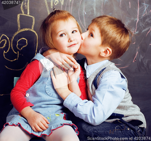 Image of little cute boy kissing blonde girl in classroom at blackboard, first school love, lifestyle people concept 