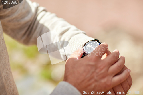 Image of senior man checking time on wristwatch outdoors