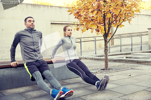 Image of couple doing triceps dip on city street bench