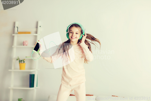 Image of girl jumping on bed with smartphone and headphones