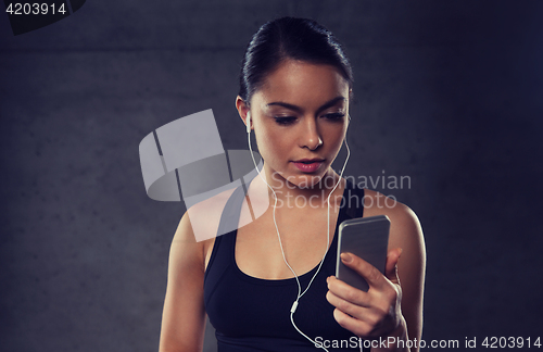 Image of woman with smartphone and earphones in gym