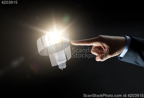 Image of businessman pointing finger to lightbulb over dark