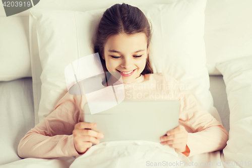 Image of happy girl lying in bed with tablet pc at home